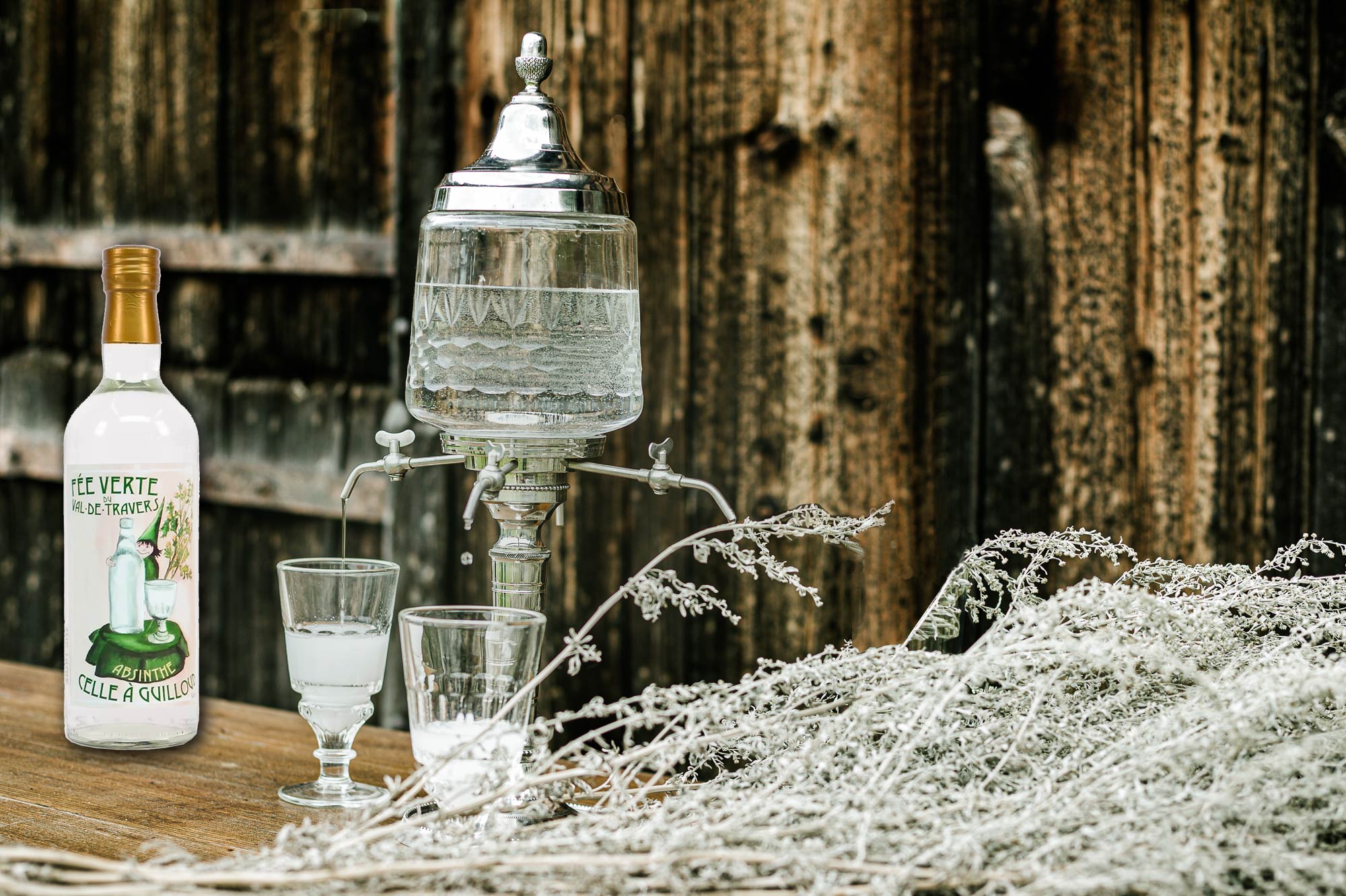 Flasque et verres à absinthe sur une table, bouteille intitulée absinthe originaire du Val-de-Travers, avec fontaine d'absinthe et décor givré. absinthe alcool origine.